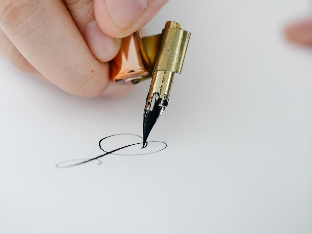 Une main trace une lettre à la plume sur du papier blanc